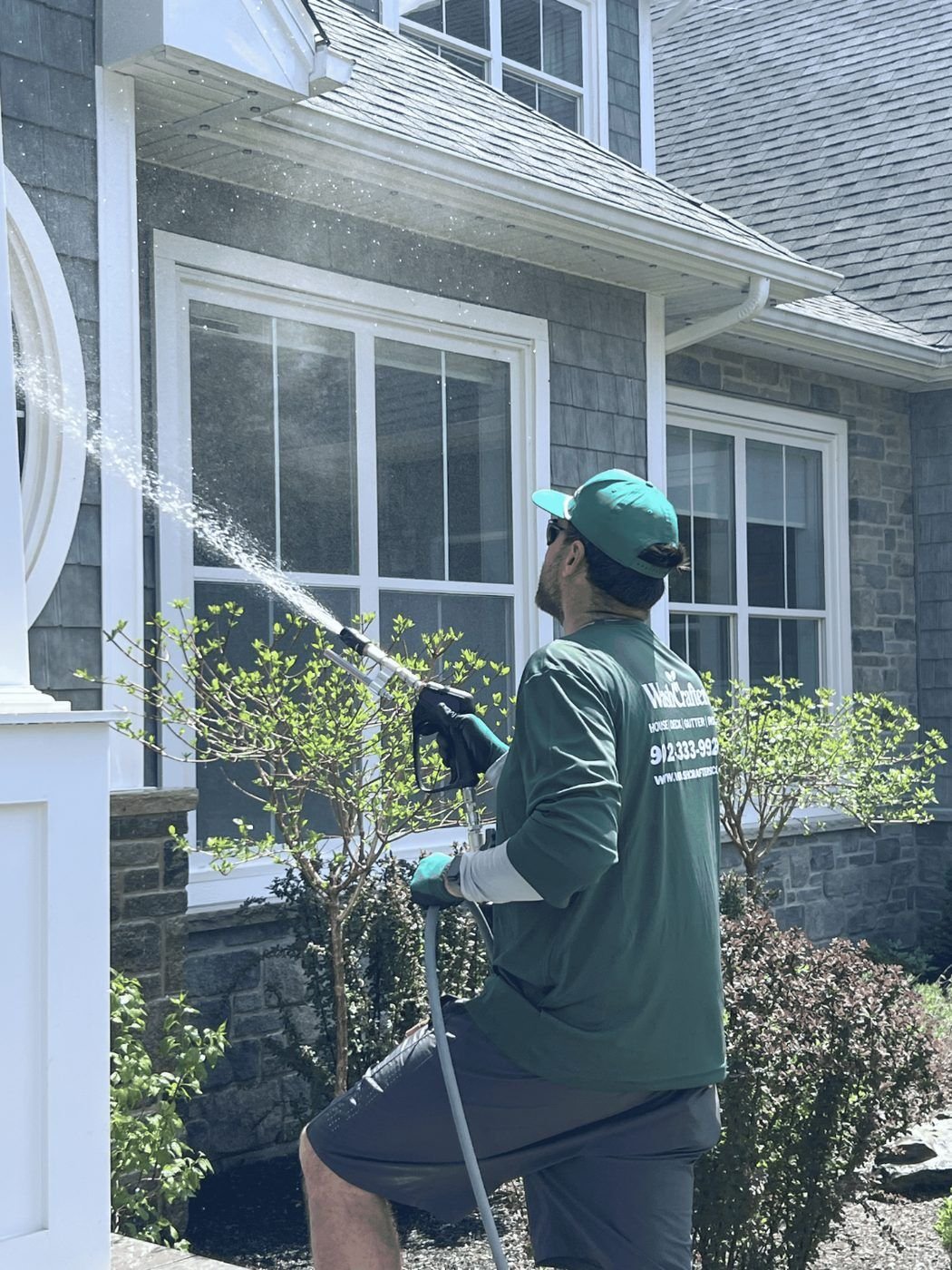 WashCrafters technician soft washing a home exterior
