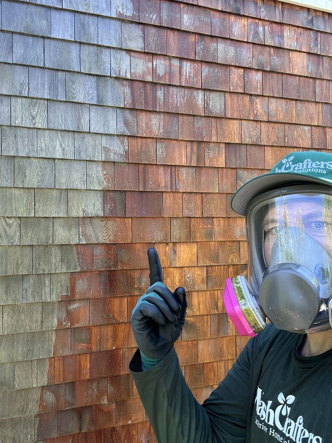 WashCrafters technician in full respirator PPE applying brightening treatment to cedar shake siding, showing the dramatic colour transformation